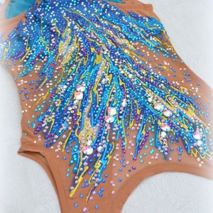 May include: A brown leotard with a blue, yellow, and purple design. The leotard is covered in rhinestones and has a sheer fabric. The leotard is for gymnastics or dance.