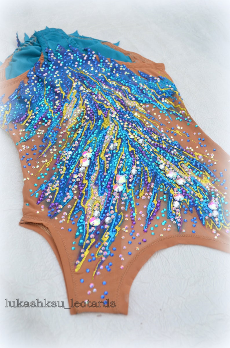 May include: A brown leotard with a blue, yellow, and purple design. The leotard is covered in rhinestones and has a sheer fabric. The leotard is for gymnastics or dance.