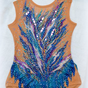 May include: A teal and brown leotard with a blue and gold design. The leotard is covered in rhinestones and sequins.