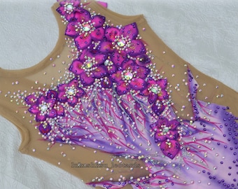 Peut inclure: Justaucorps de gymnastique avec un haut en résille nude et un design vibrant. Le justaucorps présente de grandes appliques de fleurs magenta avec des strass étincelants. La partie inférieure passe du violet au blanc, avec des strass supplémentaires.