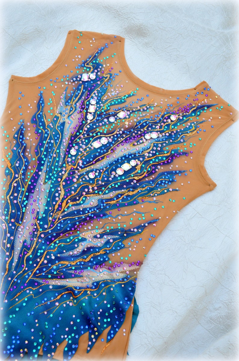 May include: A brown leotard with a blue, teal, and gold design. The leotard is covered in rhinestones and sequins.