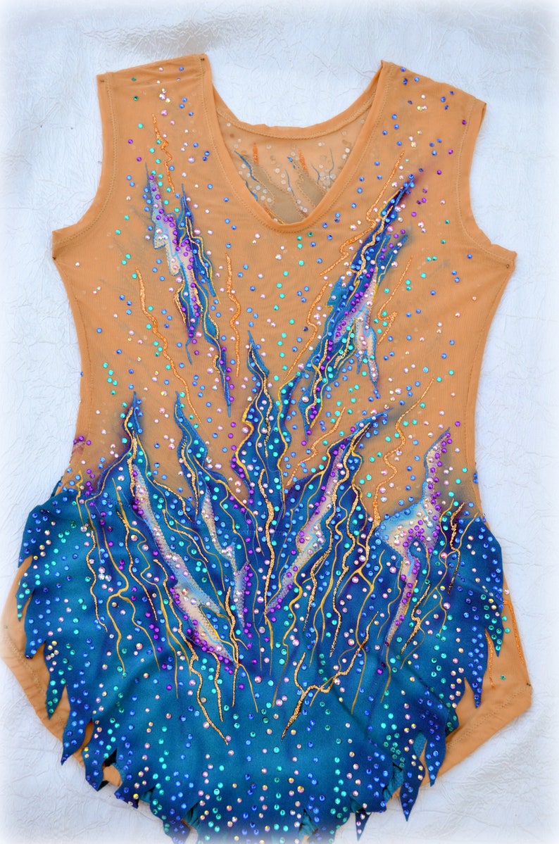 May include: A nude-colored leotard with a blue and gold design. The leotard is covered in rhinestones and has a V-neck.