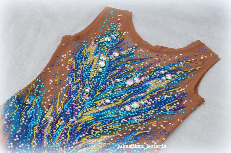 May include: A brown leotard with a blue, gold, and purple design. The leotard is covered in rhinestones and sequins.