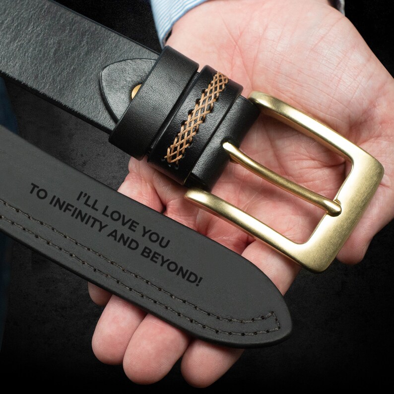 May include: Black leather belt with a gold-colored buckle. The belt features decorative stitching and a woven leather detail. The text "I'LL LOVE YOU TO INFINITY AND BEYOND!" is engraved on the belt.