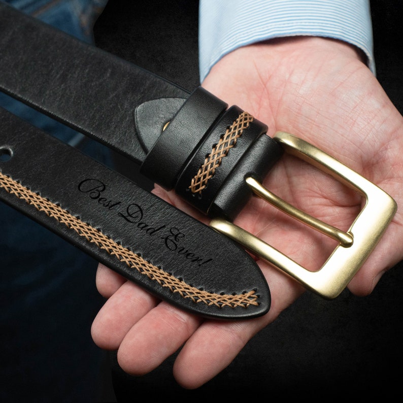 May include: Black leather belt with a gold-colored buckle. The belt features decorative stitching in a lighter brown color. The text "Best Dad Ever!" is engraved on the belt.