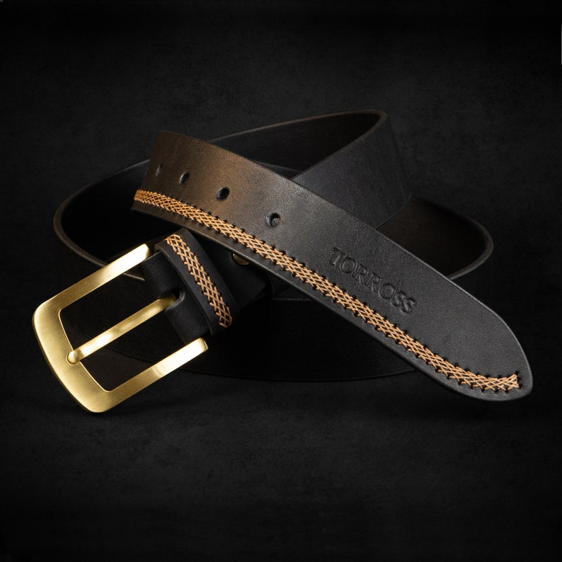 May include: Black leather belt with a gold-colored buckle. The belt features decorative stitching in a lighter brown color along the edges. The brand name "TORROSS" is embossed on the belt.