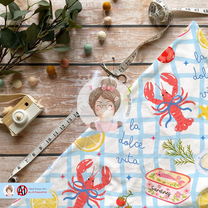 May include: A patterned fabric with a blue and white check design, showcasing red lobsters, lemons, and the words "la dolce vita." A measuring tape, scissors, and a toy camera are also present. The fabric is likely for crafts or home decor.