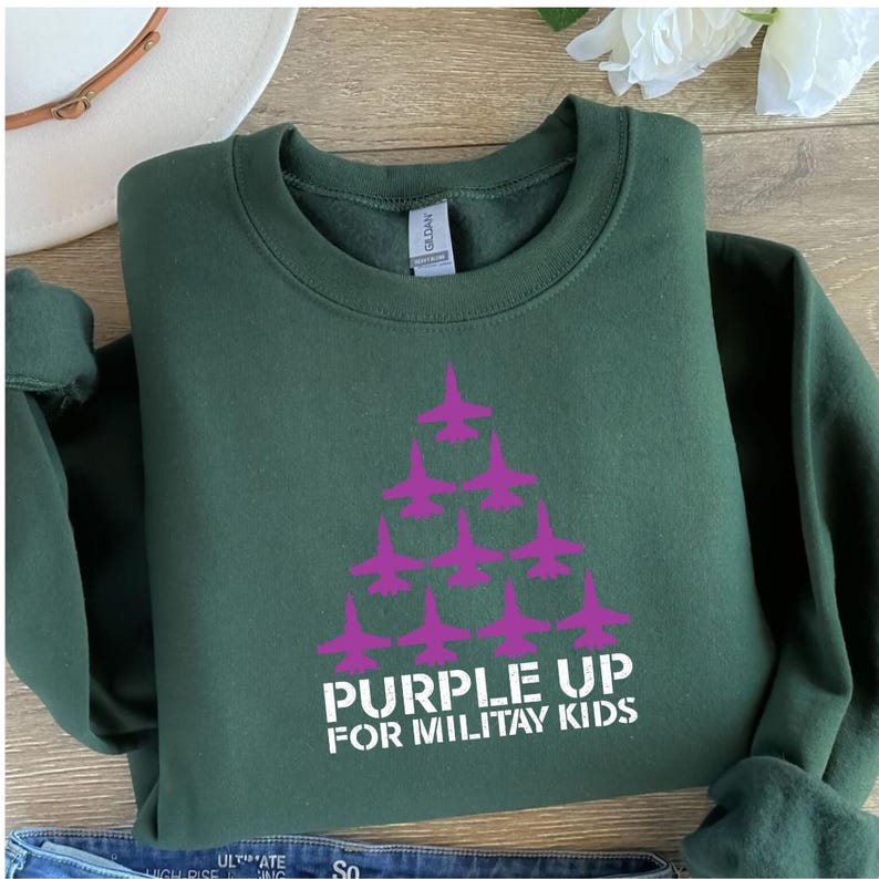 May include: A dark green sweatshirt with a white graphic of a purple airplane formation and the text "Purple Up for Military Kids".