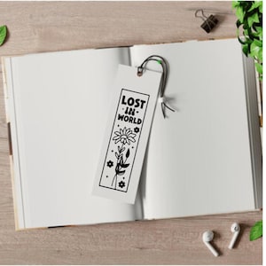 K&ouml;nnte beinhalten: Ein wei&szlig;es Lesezeichen mit einer schwarz-wei&szlig;en Illustration einer Blume und dem Text "LOST IN WORLD" mit einem Herzsymbol.