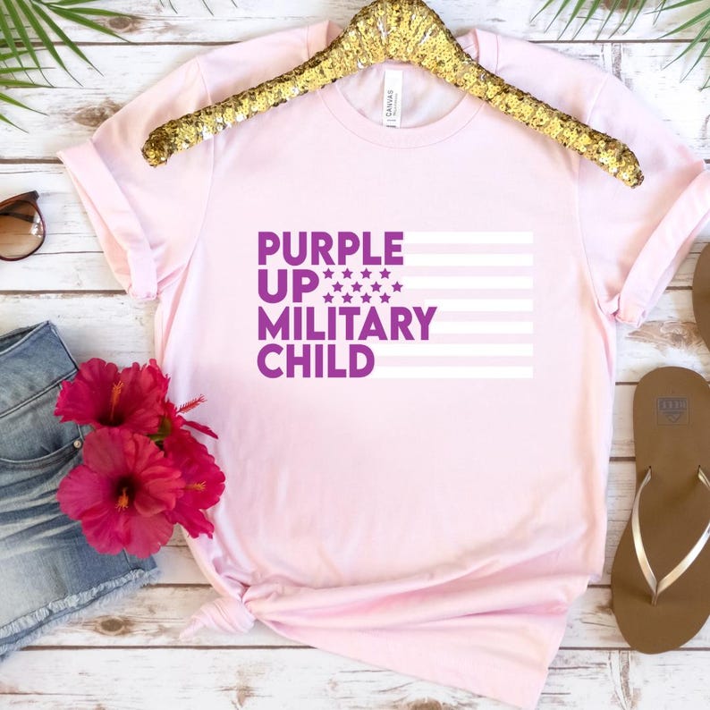 May include: Pink t-shirt with a purple graphic that says "Purple Up Military Child" with a white and purple American flag design.