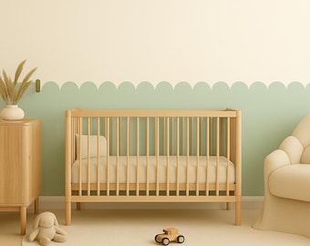 Op de afbeelding: Een licht houten babybedje met een beige matras en kussen. Een houten speelgoedauto en een knuffelkonijn liggen op het crèmekleurige tapijt. Een houten kast met een vaas met gedroogde planten en een beige fauteuil maken de kinderkamer compleet.