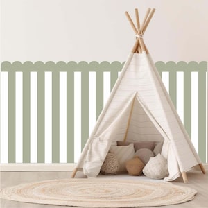 Pode incluir: Uma tenda tipi de lona branca com postes de madeira, colocada sobre um chão de madeira clara. Dentro da tenda existem várias almofadas decorativas. Um tapete redondo e tecido está colocado em frente à tenda. O fundo apresenta uma parede listrada verde e branca.
