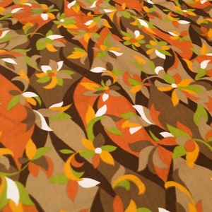 Op de afbeelding: Een bruine stof met een herhalend patroon van gestileerde bloemen in tinten oranje, geel, groen en wit.