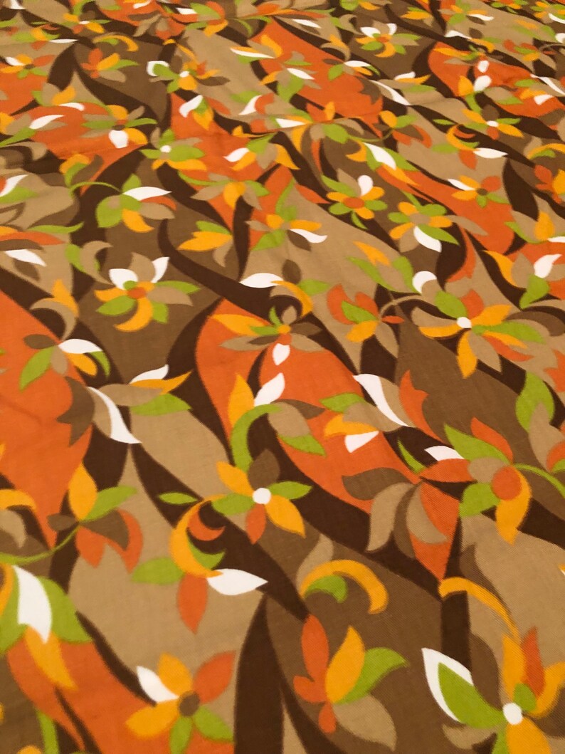 Op de afbeelding: Een bruine stof met een herhalend patroon van gestileerde bloemen in tinten oranje, geel, groen en wit.