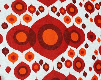 May include: A white fabric with a repeating pattern of red and orange circles within teardrop shapes. The circles have a dark red outline.
