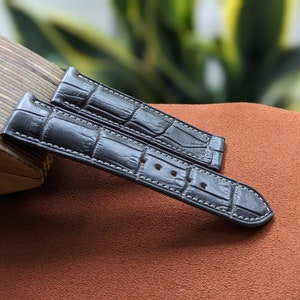 Peut inclure: Deux bracelets de montre en cuir noir avec un motif crocodile et des coutures blanches.
