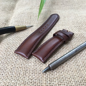 May include: Two brown leather watch straps with stitching detail, and a metal watch band tool.