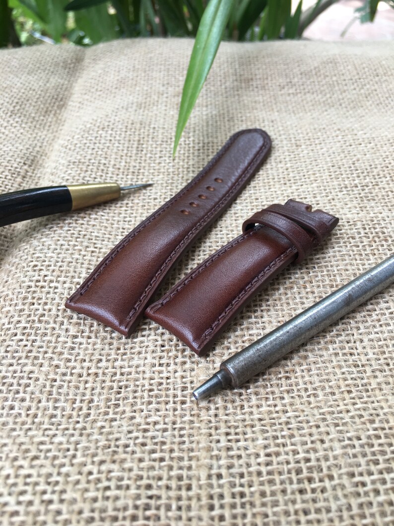 May include: Two brown leather watch straps with stitching detail, and a metal watch band tool.