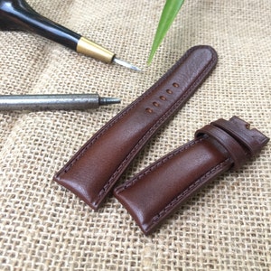May include: Two brown leather watch straps with stitching detail. The straps are laid out on a burlap fabric background.