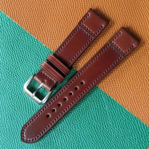 May include: Two brown leather watch straps with stitching detail. One strap has a silver buckle.