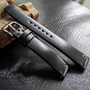 May include: Two black leather watch straps with silver hardware. The straps are laid out on a dark surface.