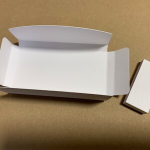May include: A white cardboard box with a lid and a separate white cardboard piece. The box is open and the lid is folded back.