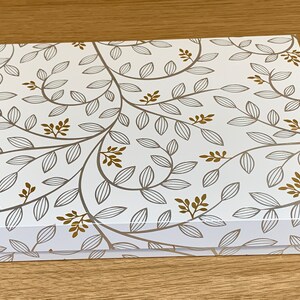 May include: A white gift box with a gold and gray floral pattern. The box has a lid and is closed.