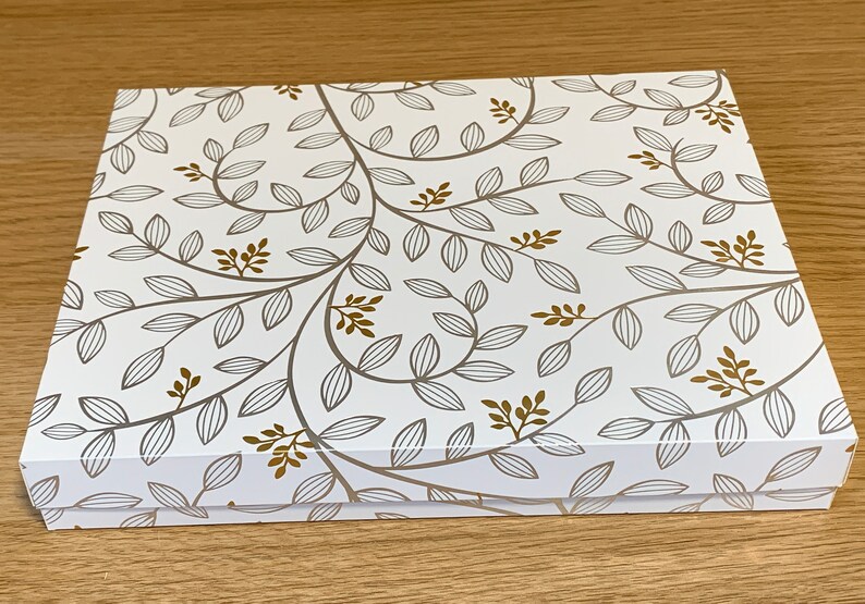 May include: A white gift box with a gold and gray floral pattern. The box has a lid and is closed.