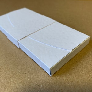May include: A white cardboard box with a curved flap. The box is closed and appears to be empty.