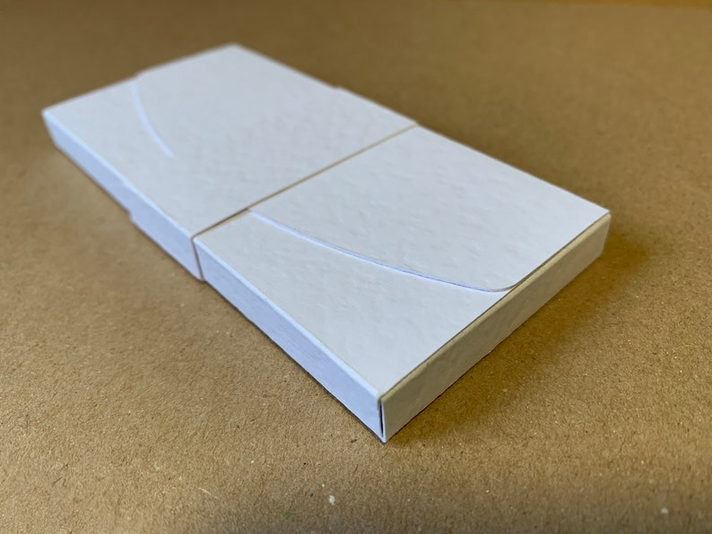 May include: A white cardboard box with a curved flap. The box is closed and appears to be empty.