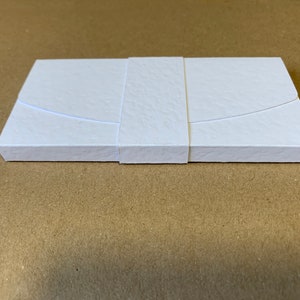 May include: A white box with a textured surface and a white ribbon tied around it.