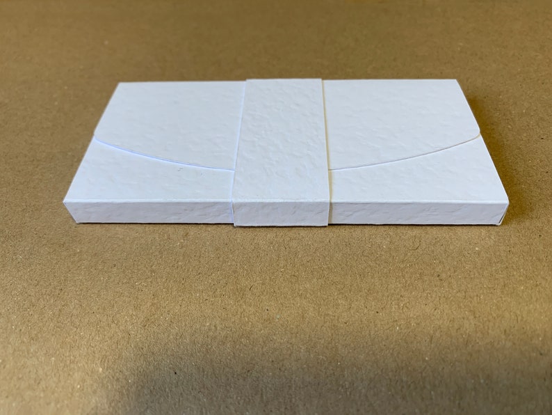 May include: A white box with a textured surface and a white ribbon tied around it.