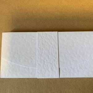 May include: A white envelope with a textured surface and a curved flap. The envelope is made of thick paper and has a modern design.