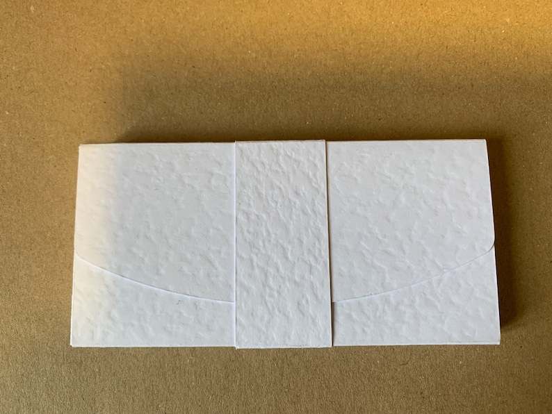 May include: A white envelope with a textured surface and a curved flap. The envelope is made of thick paper and has a modern design.