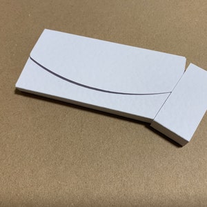 May include: A white cardboard box with a curved flap, partially open to reveal a smaller white box inside.