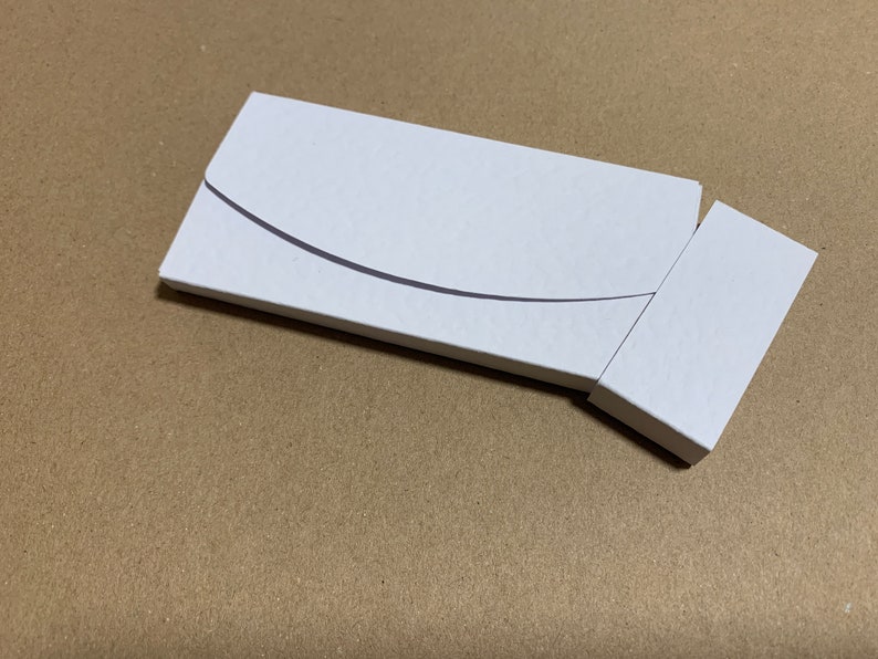 May include: A white cardboard box with a curved flap, partially open to reveal a smaller white box inside.