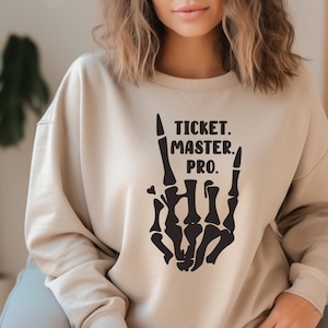 May include: A beige sweatshirt with a black skeleton hand making the rock and roll hand gesture. The text "TICKET. MASTER. PRO." is printed above the hand.