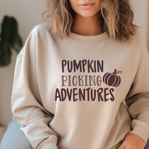May include: A beige sweatshirt with the text "Pumpkin Picking Adventures" in brown lettering and a brown silhouette of a pumpkin.