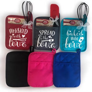 May include: Set of six oven mitts with quilted fabric and a pocket on the front. The mitts are in red, black, gray, pink, blue, and turquoise. Each mitt has a different saying on the front: "Whisked with love", "Spread the love", and "Baked with love".