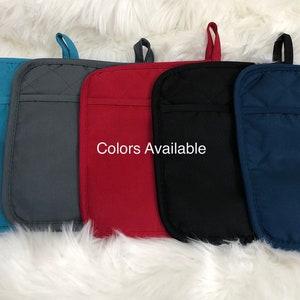 May include: Five oven mitts in different colours: teal, grey, red, black, and navy blue. The mitts are quilted and have a pocket on the back. "Colors Available" is written in white text on a red mitt.
