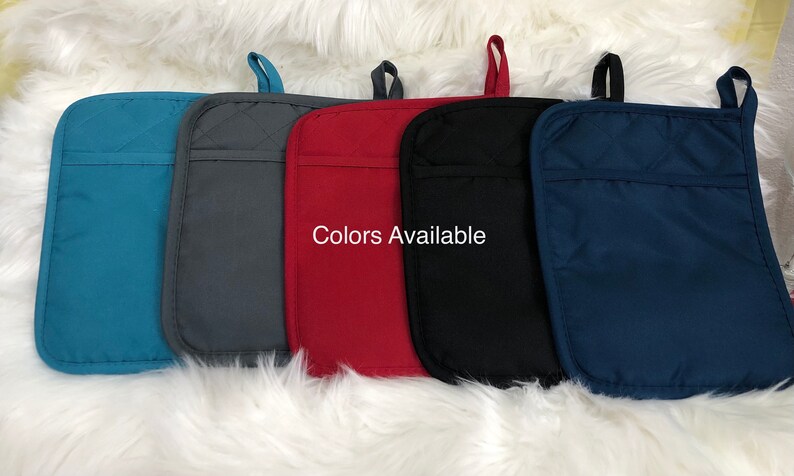 May include: Five oven mitts in different colours: teal, grey, red, black, and navy blue. The mitts are quilted and have a pocket on the back. "Colors Available" is written in white text on a red mitt.
