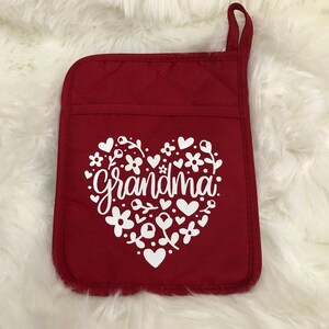 May include: Red quilted oven glove with a white heart design featuring the word "grandma" surrounded by flowers and hearts.