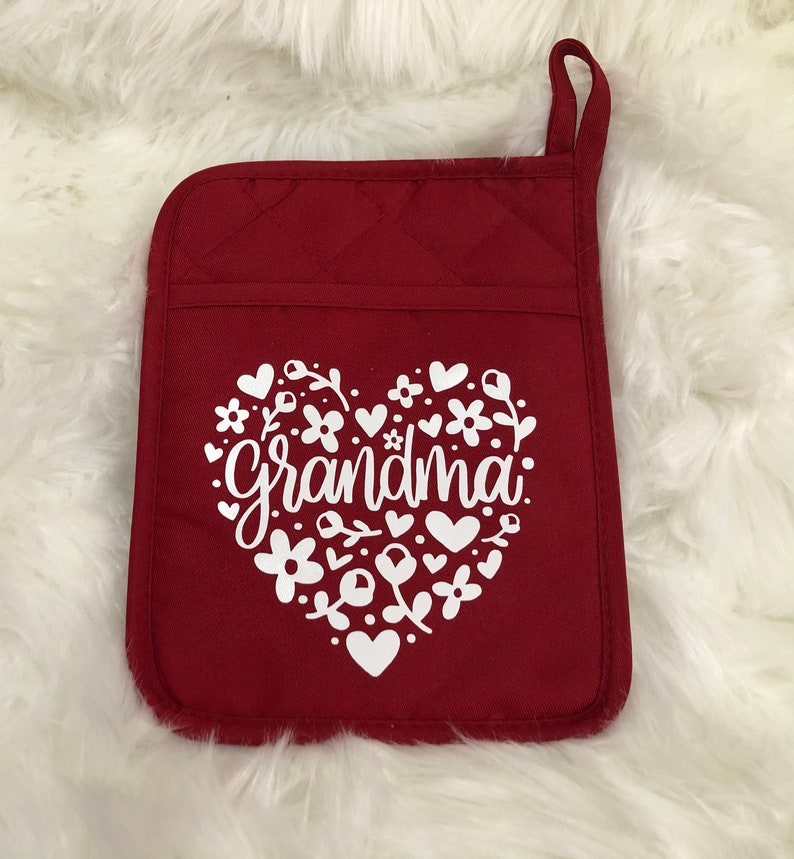May include: Red quilted oven glove with a white heart design featuring the word "grandma" surrounded by flowers and hearts.