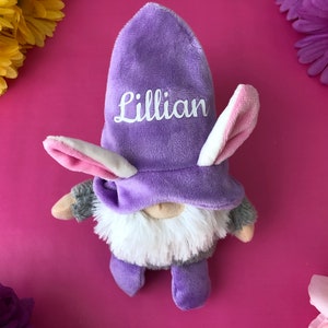 Puede incluir: Gnome morado con un gorro de conejo blanco y rosa. El gorro tiene el nombre "Lillian" bordado.