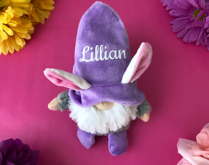 Puede incluir: Gnome morado con un gorro de conejo blanco y rosa. El gorro tiene el nombre "Lillian" bordado.