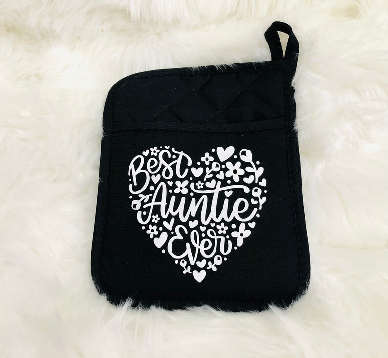 May include: Black oven mitt with a white heart design that says "Best Auntie Ever" surrounded by small white flowers and hearts.