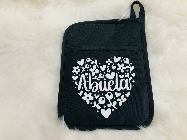 May include: Black quilted oven mitt with a white heart design. The heart features the word "Abuela" surrounded by flowers and small hearts.