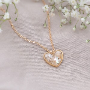 May include: A gold chain necklace with a heart-shaped pendant filled with iridescent white seashells.