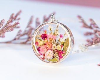 May include: A silver pendant necklace with a round glass charm containing a bouquet of pressed pink and white flowers.