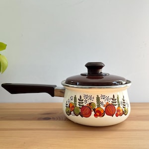 May include: Cream-coloured saucepan with a dark brown lid and handle. The pot features a decorative pattern of colourful vegetables and foliage. The handle is angled for easy grip. A vintage kitchenware item.